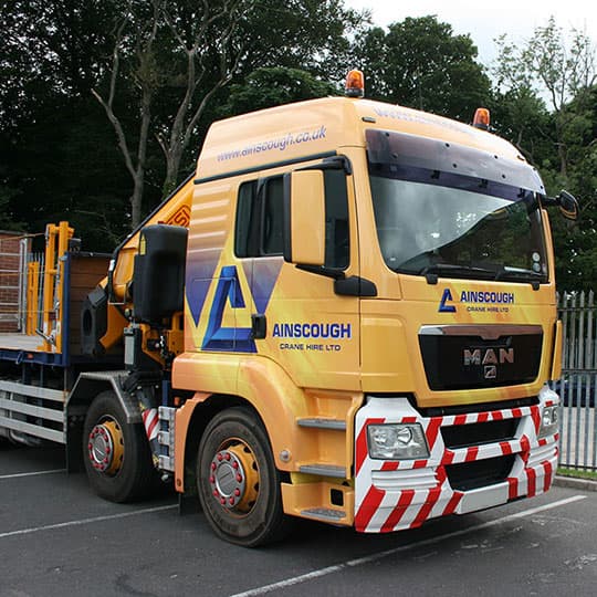 A yellow truck featuring a crane on top, with a digitally printed full wrap on its cabin